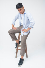 Asian man sits on a wooden stool with a serious expression, gazing downward in a moment of deep...