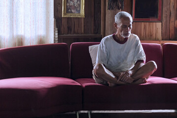 Elderly Asian man meditating on a red sofa
