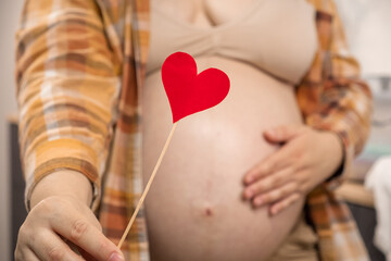 Pregnant woman holding red heart shape and feel love for unborn baby in belly. Awaiting for baby. Concept of maternity and pregnancy care