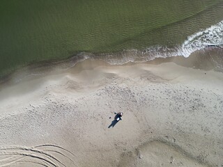 Lone figure walking on expansive sandy beach captured from drone perspective revealing coastal...
