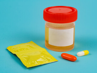 Urine sample container with medicine capsules isolated on teal background. Medical concept