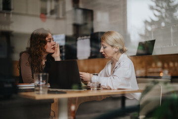Two women engage in a focused business discussion within a casual co working cafe setting,...