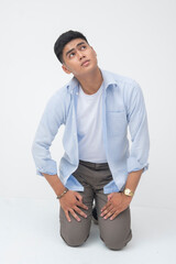 Southeast Asian man kneels with hands on thighs, looking up toward the sky with a helpless,...