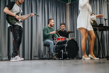 Musicians rehearsing with various instruments including a guitar, drums, and keyboard while a...