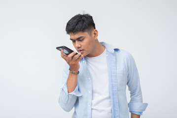 Southeast Asian man leans toward smartphone with serious expression, furrowed eyebrows, and angry...
