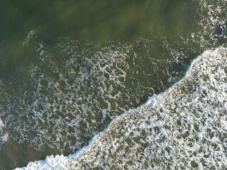 High-angle aerial view of ocean waves breaking with distinctive white foam patterns against dark...