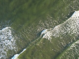Aerial view of pristine ocean waves crashing against rocky coastal shore creating white foam...