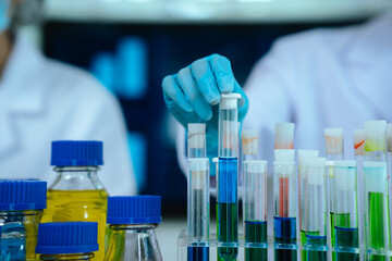 Scientists in lab coats and gloves pour blue liquid from one test tube to another to perform chemical experiments in a laboratory environment.