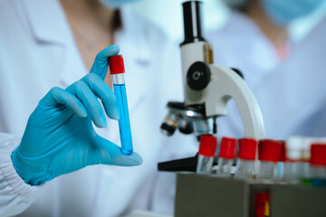 Scientists in lab coats and gloves pour blue liquid from one test tube to another to perform...