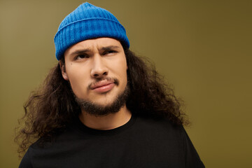 Handsome young bearded man with curly hair wearing a blue beanie in a studio setting