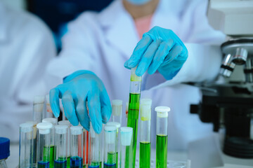 Scientists in lab coats and gloves pour blue liquid from one test tube to another to perform...