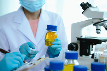 Scientists in lab coats and gloves pour blue liquid from one test tube to another to perform...