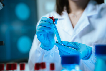 Scientists in lab coats and gloves pour blue liquid from one test tube to another to perform...