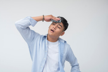 Southeast Asian man appears tired and overwhelmed, wiping sweat from his temple with mouth open and...