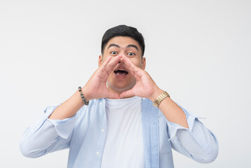 Young Filipino man with wide eyes and open mouth shouts joyfully with hands cupped around his face, full of excitement, energy, and cheerful expression in a studio portrait.