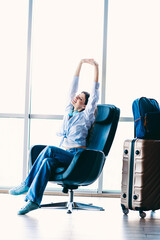 Passenger woman patiently sitting and stretching in an airport while traveling with luggage waiting...