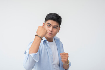 Confident Southeast Asian man raises his clenched fist in a bold, taunting stance with direct eye...