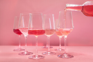 Rose wine poured from a bottle into a glass, a variety of hues and tints, side view on a pink background, many wineglasses