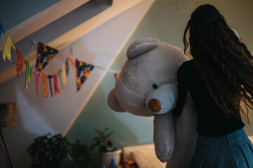 A young woman interacts with a large teddy bear during a lively home birthday celebration decorated...