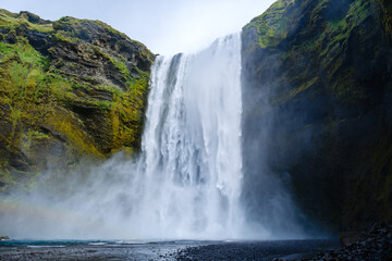 Skogafoss Waterfall displays a breathtaking plunge surrounded by verdant cliffs. Mist drifts in the...