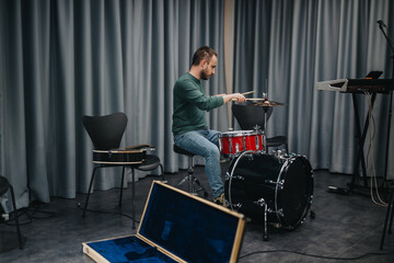 A young musician focused on playing drums in a music studio surrounded by instruments.