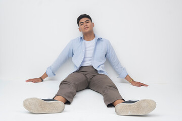 Southeast Asian man sitting on the floor, legs extended, leaning back against the wall with a...