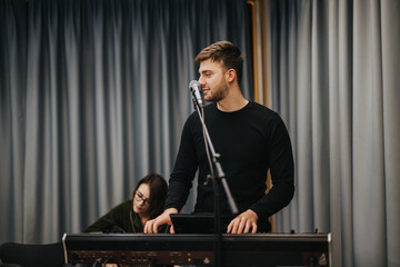 A talented young musician practices on his keyboard while singing into a microphone. The setting is...