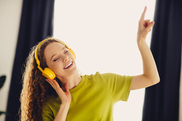 Positive woman wearing headphones while enjoying music and dancing in a bright modern home with positive energy