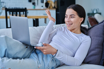 Young teenage girl using laptop for video chat lying on sofa at home