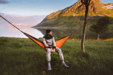 Man chilling in hammock traveling solo in Norway outdoor camping gear summer vacations traveler...