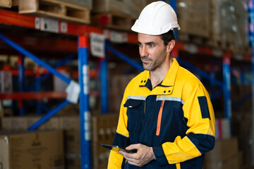 adult male warehouse professional wearing yellow uniform using digital tablet to update inventory...