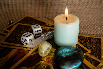 A soft blue candle burns on tarot cards, with dice, quartz, citrine, and labradorite on burlap. A...
