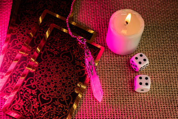 Tarot cards with vivid illustrations lie on burlap, with a quartz pendulum and a lit candle. A...
