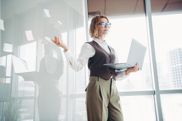 Confident businesswoman presenting ideas in modern office setting using laptop and brainstorming...