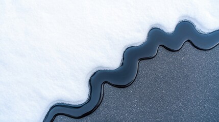 Close-up of black liquid spilling on white snow forming wavy border pattern on asphalt surface