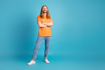 Cheerful young man in casual orange t-shirt posing against a bright blue background showcasing stylish and trendy aesthetics