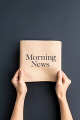 Hands holding folded newspaper titled Morning News on dark background, top view minimal composition