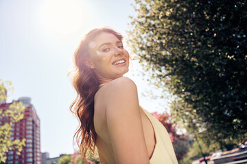 Young woman enjoying a sunny day outdoors in a stylish dress, smiling happily in an urban park...