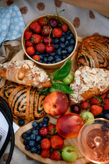 Summer picnic with fresh berries, fruits, almond croissants, and rosé wine on a cozy blanket. Flat lay top view, bright and seasonal outdoor setup.