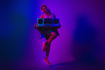 Vibrant portrait of a young woman in neon lighting holding a boombox showing modern style and...