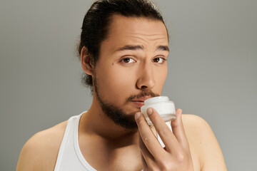 Young man applies skincare cream with a confident look in minimalistic setting