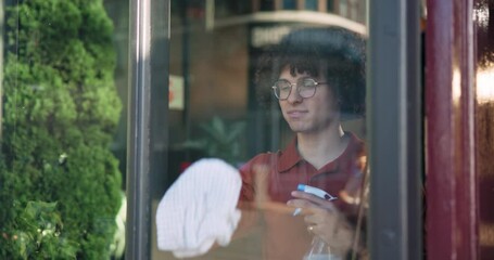 Cleaning, spray bottle and window with man in coffee shop for appearance, hygiene or opening. Bacteria, disinfectant and wiping glass with waiter in cafe or restaurant for hospitality or service