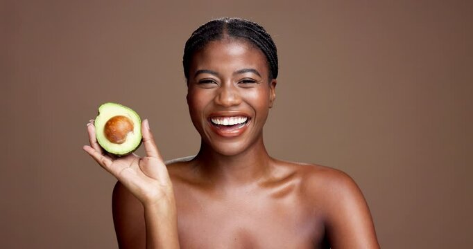 Black woman, avocado and face in studio for beauty, happy and nutrition for skincare by background. African girl, model and smile in portrait for wellness benefits, fruit diet and space in Nigeria
