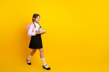 Charming schoolgirl in uniform carrying book and plants, smiling brightly against a solid yellow...