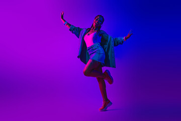 Young woman dancing under vibrant neon lighting, celebrating nightlife and fashion in stylish...