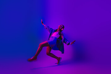 Vibrant young woman dancing in neon purple and blue lighting, showing joy and excitement in trendy...