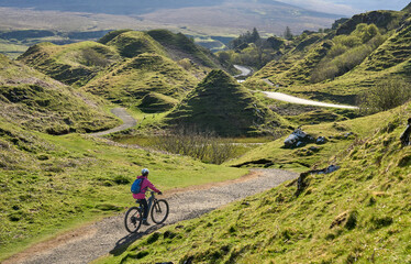 Fototapeta premium active woman riding her electric mountain bike in the spectacular volcabinic landscape of Glen Fairy on the Isle of Skye in Scotland, UK