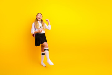Cheerful schoolgirl enjoying her school break while holding a phone against a vibrant yellow...