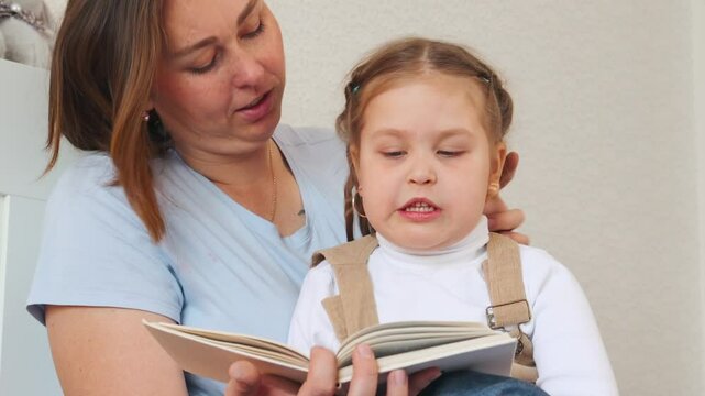 Quiet moment between mom and daughter while reading together in a bedroom. Early education and bonding in a loving indoor setting. Close up.