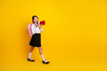 Cheerful young girl in a stylish school uniform holding a red megaphone and smiling against a bright yellow background.